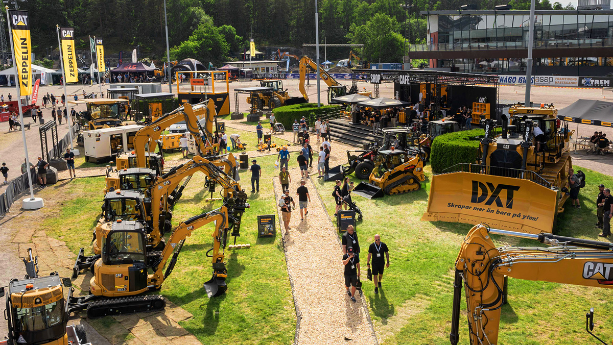 Mässmonter i sommarväder med gula entreprenadmaskiner från Cat och besökare.
